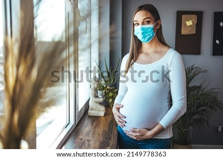 Young beautiful pregnant woman in medical surgical mask and white t-shirt on quarantine at home. Coronavirus, virus, isolation, stay at home.