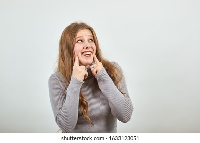 A Young Beautiful Red Haired Woman In Gray Sweater Insincerely Forced Fake Laugh Holding Her Index Fingers On Cheeks