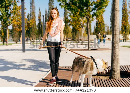 young beautiful red-haired girl in a trendy pink scarf walking with her dog in the park