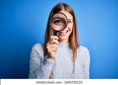 Young Beautiful Redhead Detective Woman Using Magnifying Glass Over Isolated Blue Background With A Happy Face Standing And Smiling With A Confident Smile Showing Teeth