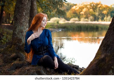 Young beautiful redhead girl sitting near the lake and smiling
