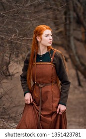 Young beautiful redhead viking woman in brown woolen historical viking dress forest background