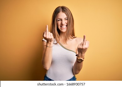 Young beautiful redhead woman wearing casual t-shirt over isolated yellow background Showing middle finger doing you bad expression, provocation and rude attitude. Screaming excited