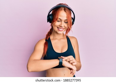 Young Beautiful Redhead Woman Wearing Gym Clothes, Using Headphones And Smart Watch Smiling With A Happy And Cool Smile On Face. Showing Teeth. 