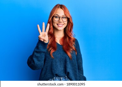 Young beautiful redhead woman wearing casual sweater and glasses over blue background showing and pointing up with fingers number three while smiling confident and happy.  - Powered by Shutterstock