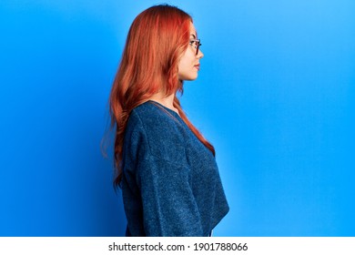 Young Beautiful Redhead Woman Wearing Casual Sweater And Glasses Over Blue Background Looking To Side, Relax Profile Pose With Natural Face With Confident Smile. 