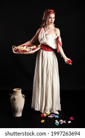 古代の白と赤のギリシャのコーチュメを着た若い美しいローマのニンフの女性モデルが、スタジオで授乳用の赤ちゃんの写真を撮る