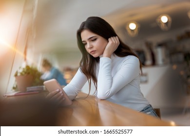 Young Beautiful Sad Woman Checking Her Smarphone Looking Upset While Sitting In The Cafe During Lunch Break, Tough Life Concept