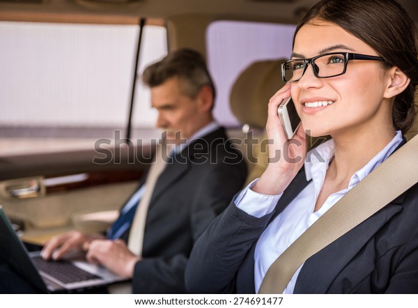 Young beautiful secretary\
in suit and glasses sitting in the car with her boss and talking on\
the phone.