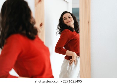  Young beautiful self confident woman in red sweater looking in the mirror proud of herself - Powered by Shutterstock