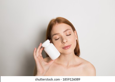 Young Beautiful Sensual Redhead Teenage Girl Portrait On White Background Holding Vitamin Bottle Mockup. Make-up Advertisement. Skin Care. Natural Cosmetics