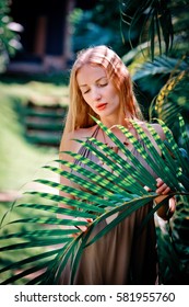 Young Beautiful And Sexy Girl Standing In The Garden And Holding A Palm Frond.