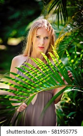 Young Beautiful And Sexy Girl Standing In The Garden And Holding A Palm Frond.