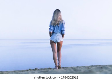 a young beautiful sexy girl stands on the lake and looks into distance at horizon in evening. rear view. Beautiful serene nature. minimalism. blonde walks on the sand on beach in morning