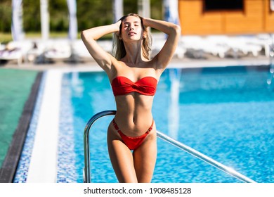 Young beautiful sexy woman standing in blue water of swimming pool. Pretty girl with log dark hair posing outdoor on a hot summer sunny day