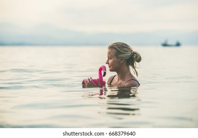 Young Beautiful Slavian Woman Tourist Swimming With Pink Flamingo Toy At Beach Near Ancient Fortress Wall And Shipyard In City Center Of Alanya, Mediterranean Turkey.