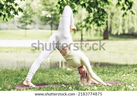 A young beautiful slender girl with long blonde hair does yoga in the summer in nature by the pond in the park.