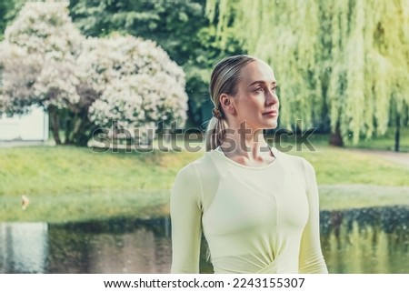 A young beautiful slender girl with long blonde hair does yoga in the summer in nature by the pond in the park