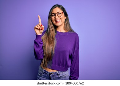 Young beautiful smart woman wearing glasses over purple isolated background pointing finger up with successful idea. Exited and happy. Number one.