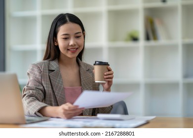 Young Beautiful smiling Asian business woman holding a coffee and laptop Placed at the wooden table at the office - Powered by Shutterstock