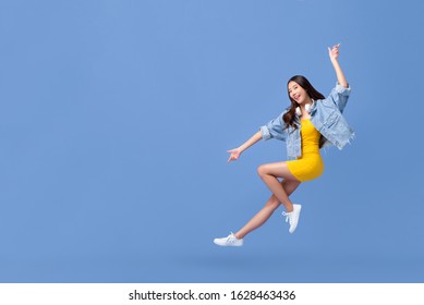 Young beautiful smiling Asian girl floating in mid-air with hand pointing up and down isolated on light blue background with copy space
