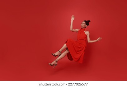 Young beautiful smiling asian woman red dress floating in mid-air relaxing isolated on red background.