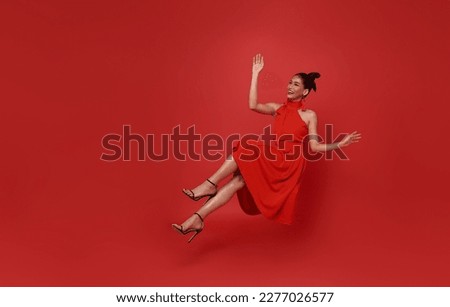 Young beautiful smiling asian woman red dress floating in mid-air relaxing isolated on red background.