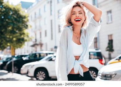 Young beautiful smiling blond woman in trendy summer clothes. Sexy carefree female posing in the street in sunny day. Positive model outdoors. Cheerful and happy, red lips. Glamorous closeup portrait 