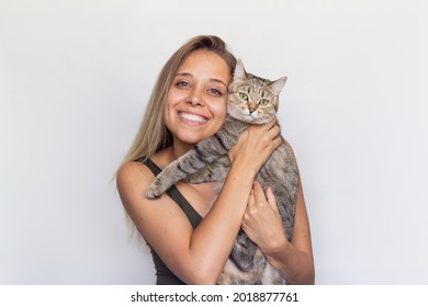 A young beautiful smiling blonde woman holds young Tabby cat in her hands isolated on a white background. Good friends. Friendship of a pet and its owner. Cuddles