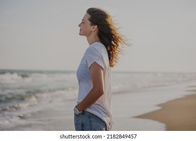 Young beautiful smiling cheerful woman in white t-shirt standing on the seashore enjoying nature
