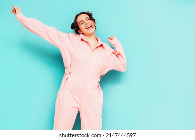 Young Beautiful Smiling Female In Trendy Summer Pink Overalls. Sexy Carefree Woman Posing Near Blue Wall In Studio. Positive Model Having Fun And Going Crazy. Cheerful And Happy. Dancing