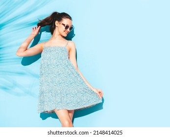 Young beautiful smiling female in trendy summer dress. Sexy carefree woman posing near blue wall in studio. Positive brunette model having fun.Cheerful and happy. Isolated. In sunglasses 