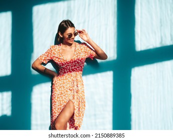 Young beautiful smiling female in trendy summer red dress. Sexy carefree woman posing near blue wall in studio. Positive model having fun. Cheerful and happy. At sunny day. Shadow from window