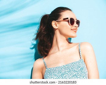 Young beautiful smiling female in trendy summer dress. Sexy carefree woman posing near blue wall in studio. Positive brunette model having fun.Cheerful and happy. Isolated
