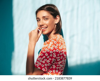 Young Beautiful Smiling Female In Trendy Summer Red Dress. Sexy Carefree Woman Posing Near Blue Wall In Studio. Positive Model Having Fun. Cheerful And Happy. At Sunny Day. Shadow From Window