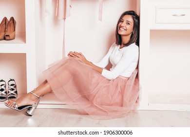 Young beautiful smiling hipster female in trendy summer dress. Sexy carefree woman sitting in pink wardrobe. Positive model having fun. Cheerful and lovely female going crazy