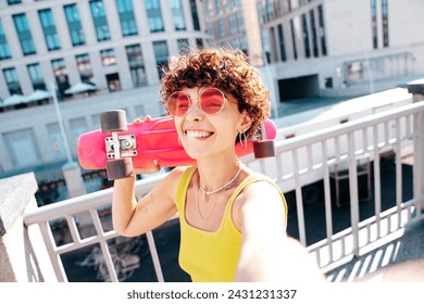 Young beautiful smiling hipster woman in trendy summer clothes. Carefree woman with curls hairstyle, posing in street. Positive model outdoors. Cheerful and happy. Holds penny skateboard, takes selfie - Powered by Shutterstock