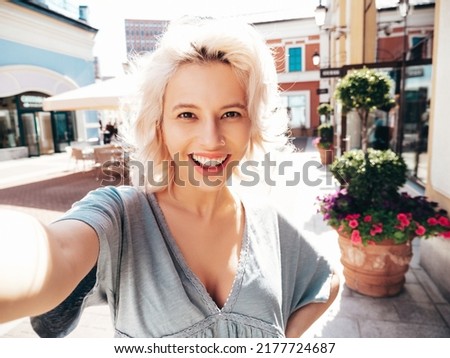 Young beautiful smiling hipster woman in trendy summer dress clothes.Sexy carefree model posing on the street background at sunset. Positive blond female outdoors. Cheerful and happy.Taking Pov selfie