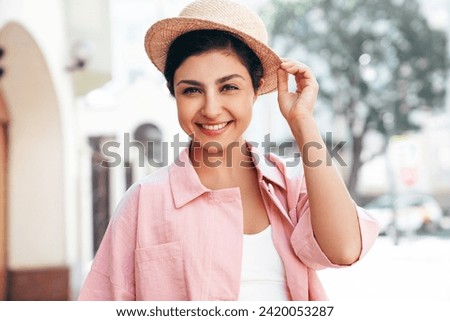 Young beautiful smiling hipster woman in trendy summer pink costume clothes. Carefree female posing in the street at sunny day. Positive model outdoors at sunset. Cheerful and happy in hat