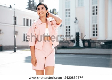 Young beautiful smiling hipster woman in trendy summer pink costume clothes. Carefree female posing in the street at sunny day. Positive model outdoors at sunset. Cheerful and happy