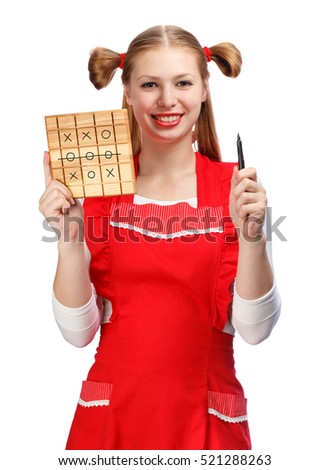 Young beautiful smiling housewife in red apron with funny ponytails holds pen and wooden cutting board with tic-tac-toe drawed on it isolated on white background.