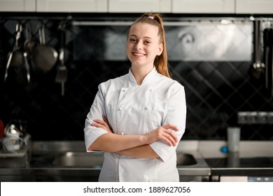 young beautiful smiling woman chef with arms crossed wearing in white suit at kitchen. Blurred background - Shutterstock ID 1889627056