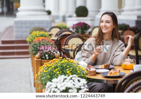 Young beautiful smiling woman drinks orange tea in a street cafe. A happy girl eats fruit cakes and drinks hot tea in the restaurant in the morning.