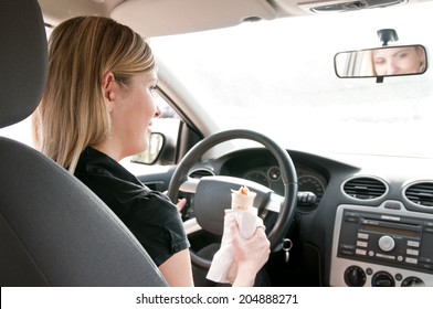 Young Beautiful Smiling Woman Driving Car And Eating Fast Food - Rear View