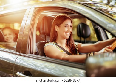 Young beautiful smiling woman driving a car.  Her cute daughter sitting on rear and enjoying. - Shutterstock ID 582848377