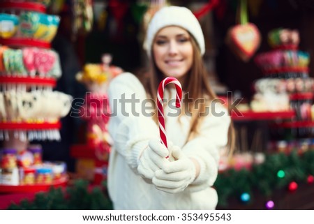 Young beautiful smiling woman holding Christmas candy cane. Model defocused. Selective focus on the object. Close up