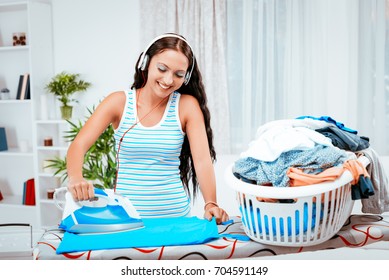 Young Beautiful Smiling Woman Ironing Clothes And Listening Music On Headphones.