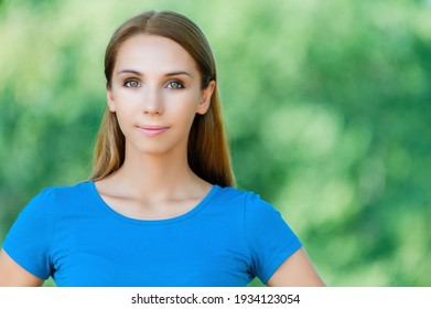 Junge schöne lächelnde Frau mit langen Haaren in einem blauen Kleid auf dem Hintergrund eines Sommergarten.