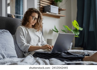 Young beautiful smiling woman working on business project using laptop while lying in bed  - Powered by Shutterstock