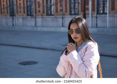 Young beautiful South American woman in a pink jacket and sunglasses, hands clasped praying. Concept religion, prayer, catholic, faith.